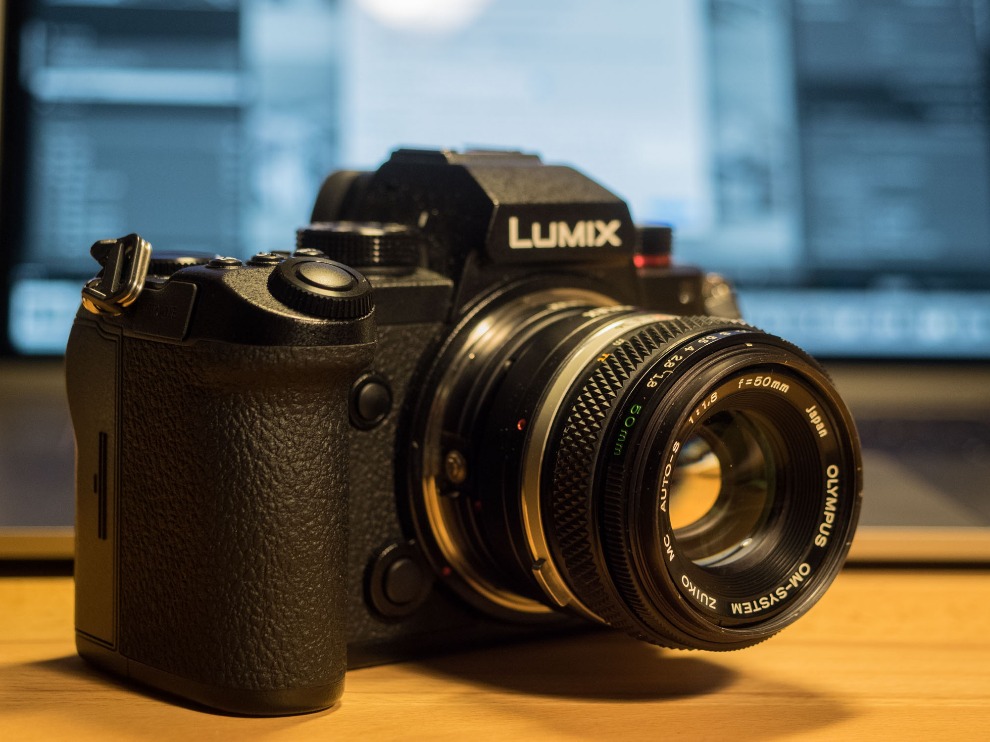 digitale Kamera (Panasonic S5) mit Vintage-Objektiv (Olympus Zuiko 1,8/50) vor Computer, auf dem das Plugin LensTagger für Lightroom läuft