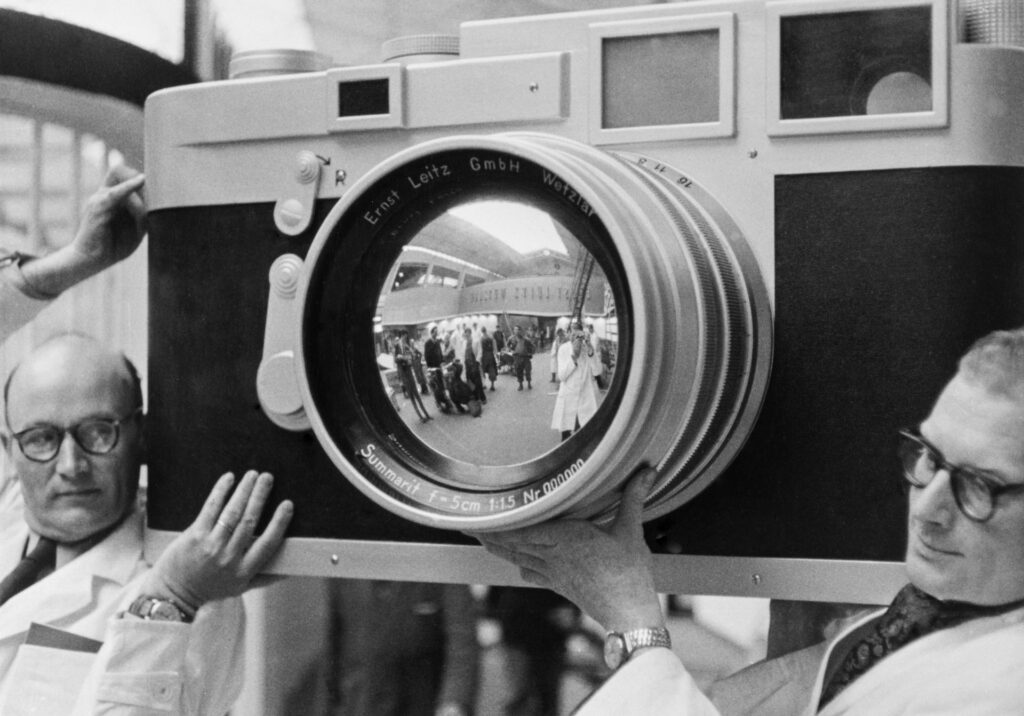 Bei der Photokina 1954 halten Männer, vermutlich Leitz-Mitarbeiter, ein überlebensgroßes Modell der Leica M3 in die Luft.