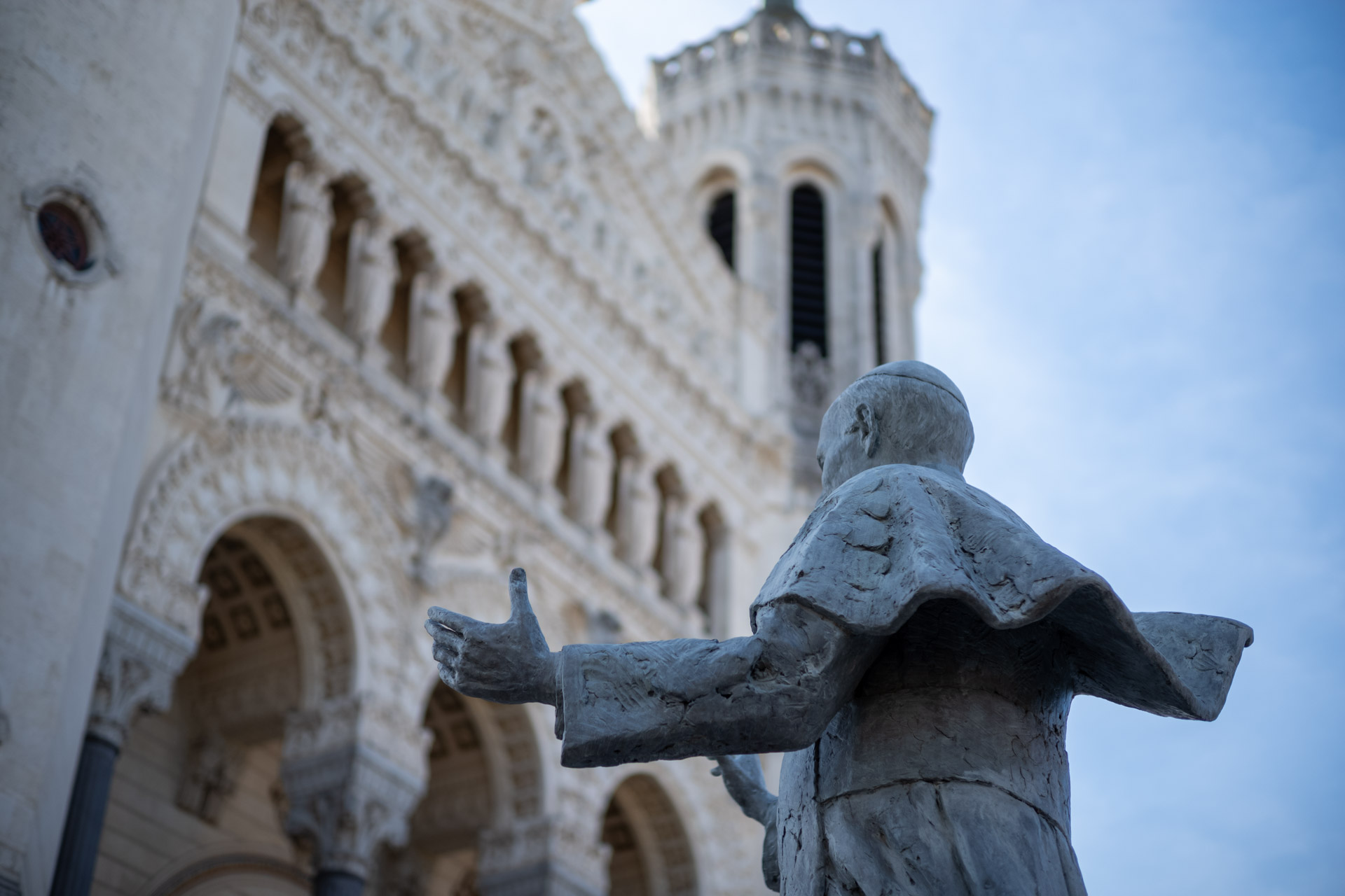 Beispielfoto mit Thypoch Simera 50/1.4: eine Statue mit ausgebreiteten Armen vor den reich verzierten Türmen der Basilique Notre-Dame de Fourvière, Lyon, Frankreich.