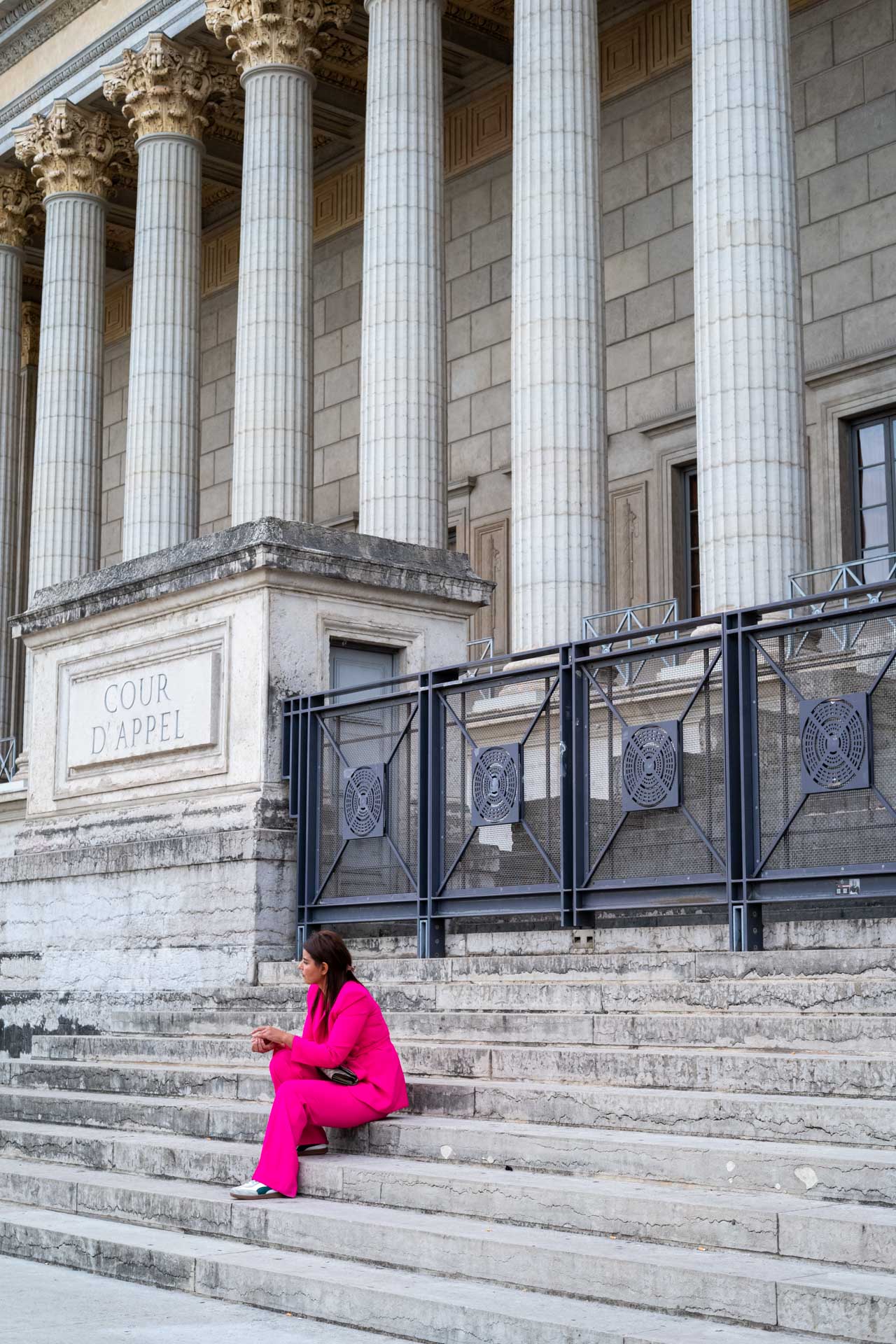Beispielfoto mit Thypoch Simera 50/1.4: eine Frau in einem knallpinken Anzug sitzt auf den Stufen der Cour d'appel de Lyon (Palais de Justice), Lyon, Frankreich.