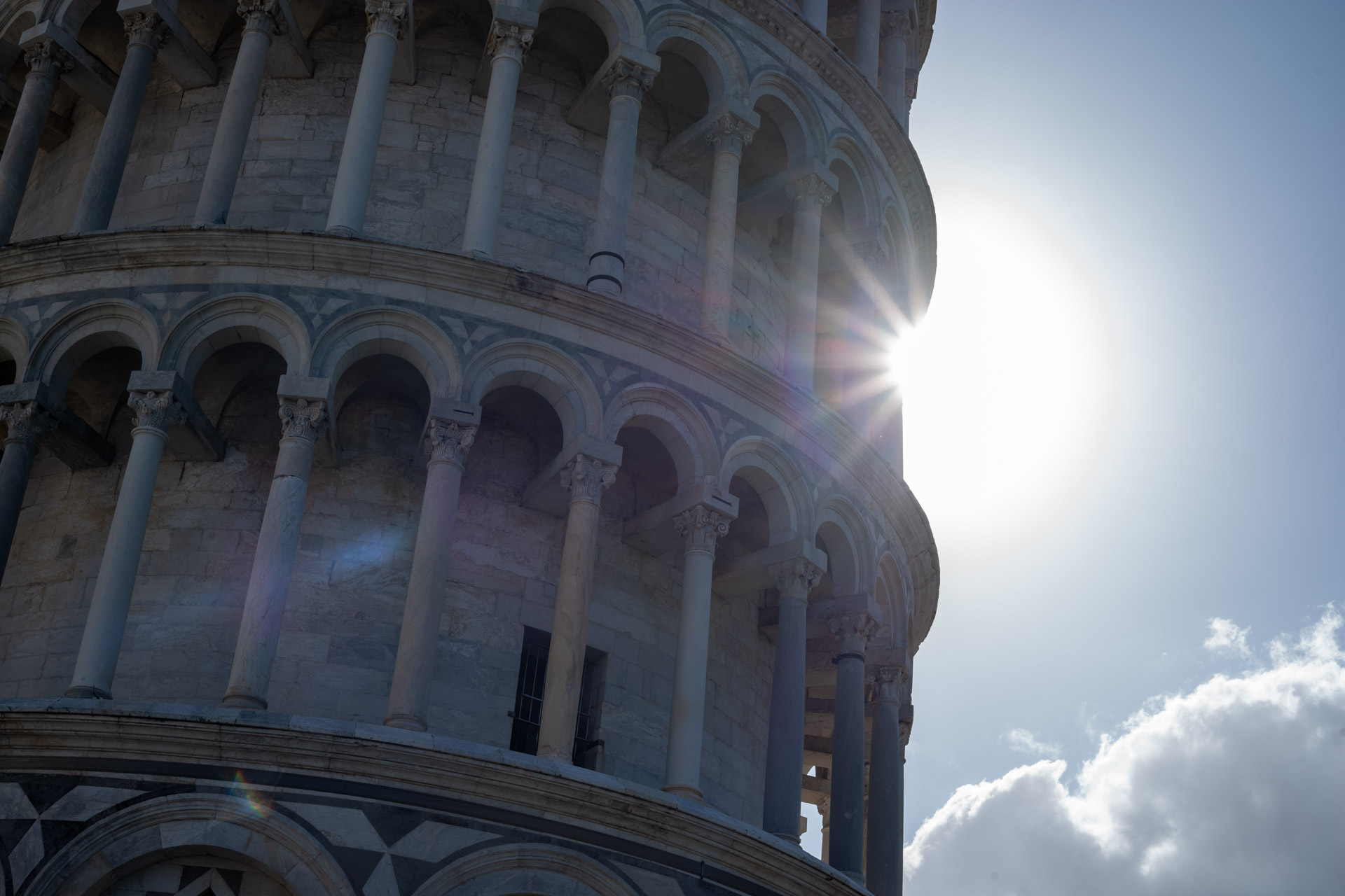 Beispielfoto mit Thypoch Simera 50/1.4: Sonnenlicht bricht zwischen den arkadengesäumten Geschossen des Schiefen Turms von Pisa, Italien.